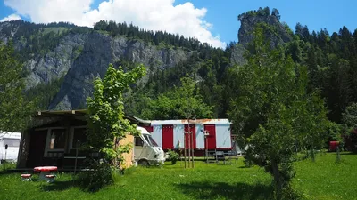 Rot-weisser Zirkuswagen mit überdachtem Vorbau auf der Wiese, dahinter der Felsturm