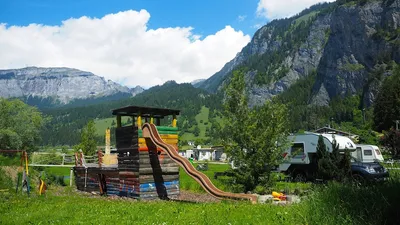 Spielturm mit Wellenrutsche, daneben ein Wohnmobil, im Hintergrund die Bergkette