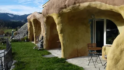Die Terrassen vor den Zimmern, Tische und Stühle vor gerundeten, verputzten Wänden, Schnee auf den Bergen