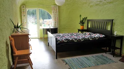 Grünes Zimmer im Erdhaus mit Doppelbett, Kommode und Tür auf die Terrasse