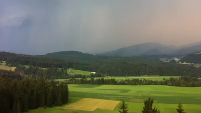Regenschauer zieht über bewaldete Hügel und Wiesen