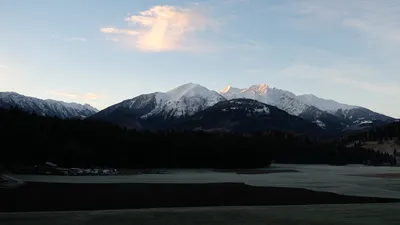 Verschneite Berggipfel im letzten Abendlicht über dem dunklen Talboden
