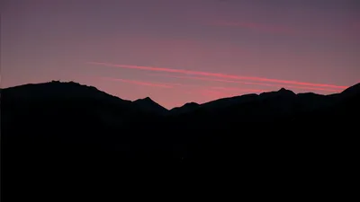 Bergkamm als Silhouette im Abendrot, darüber rot gefärbte Kondensstreifen