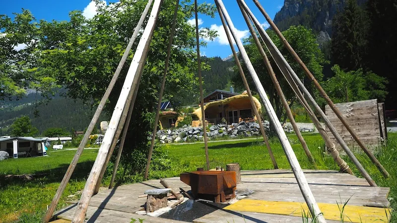 Tipi-Gestänge aus langen Stangen über einer Feuerschale auf einer Holzplattform