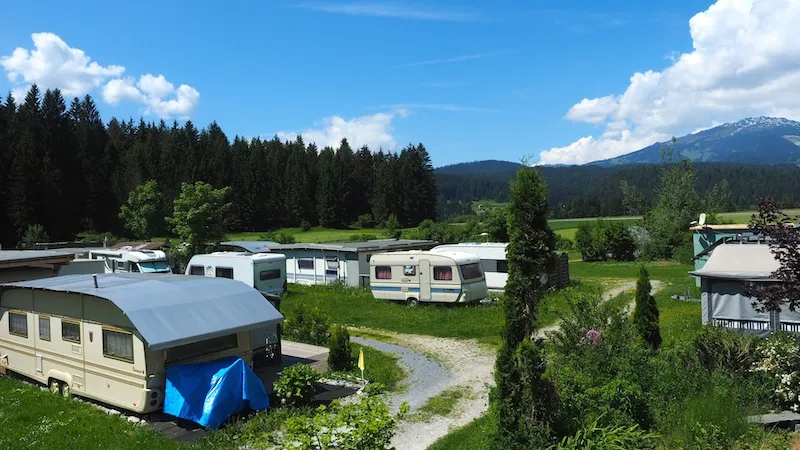 Reihe von Wohnwagen auf den Jahresplätzen, dahinter Wald und Berge