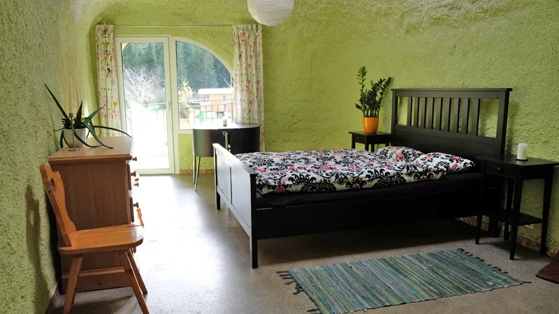 Grünes Zimmer im Erdhaus mit Doppelbett, Kommode und Tür auf die Terrasse