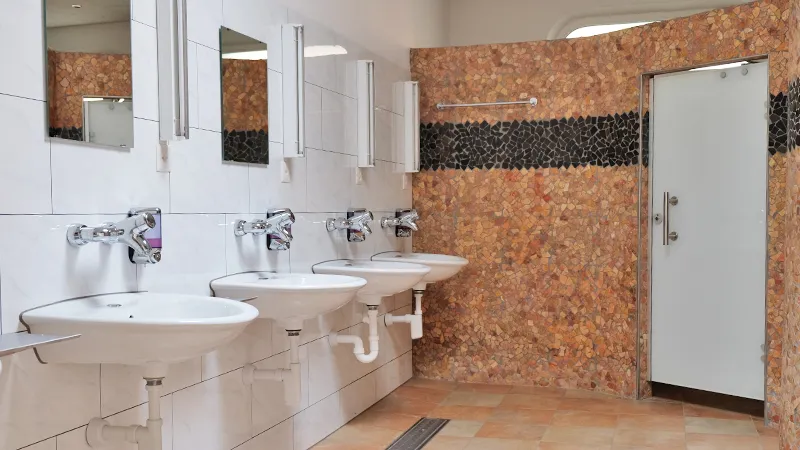 Waschraum mit vier Lavabos, Spiegeln und einer Wand aus Kieselmosaik