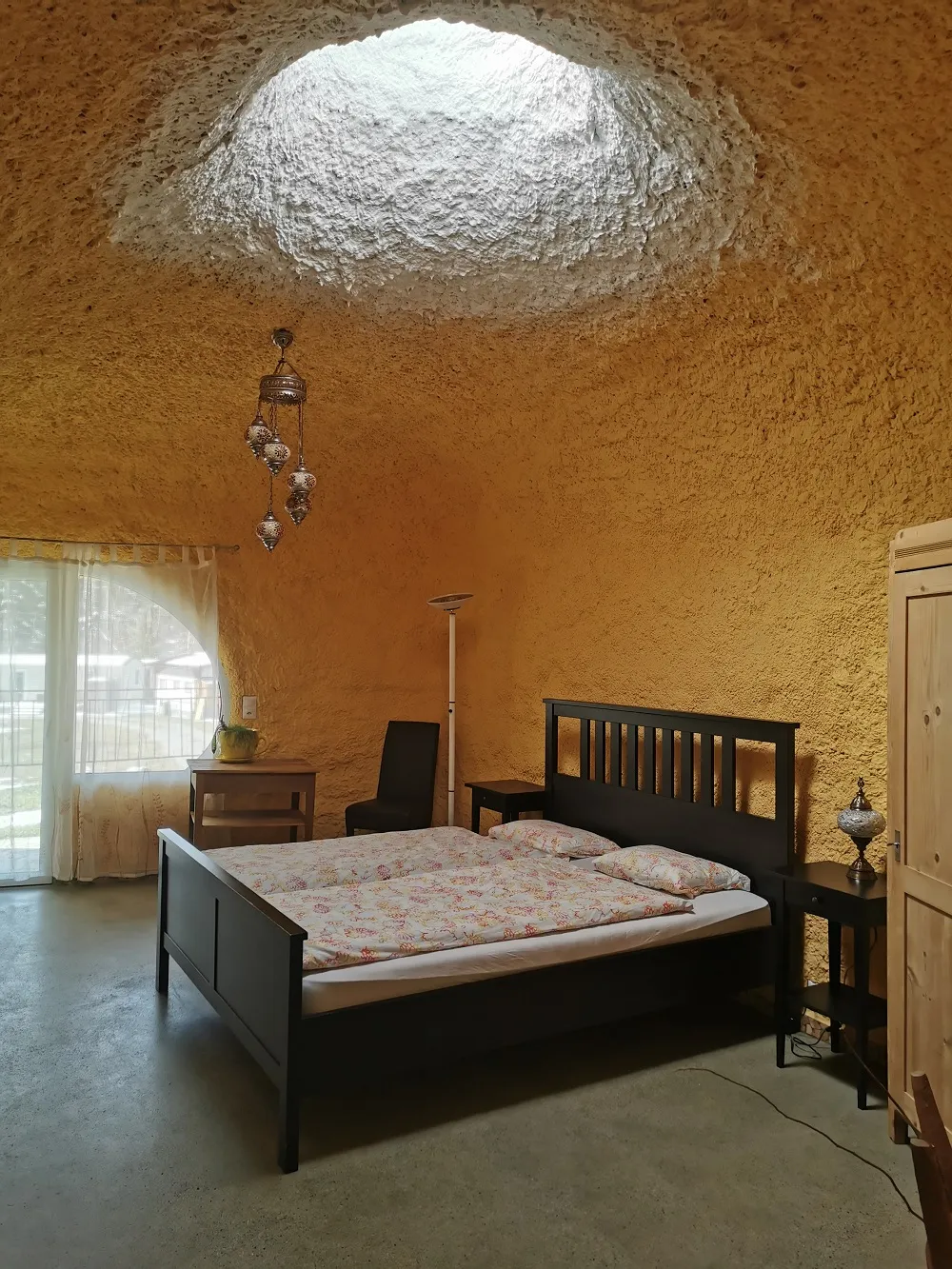 Zimmer 1 im Erdhaus: Doppelbett unter der gewölbten Decke, eine runde Lichtkuppel in der Decke, Tür auf die Terrasse