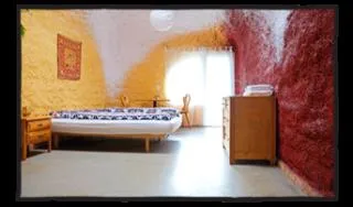 Zimmer 2 im Erdhaus: Bett vor gelber und roter Wand, daneben eine Kommode